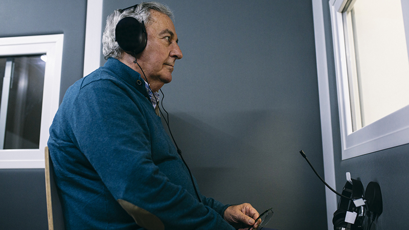 A mature person seated and wearing headphones, having a hearing test.