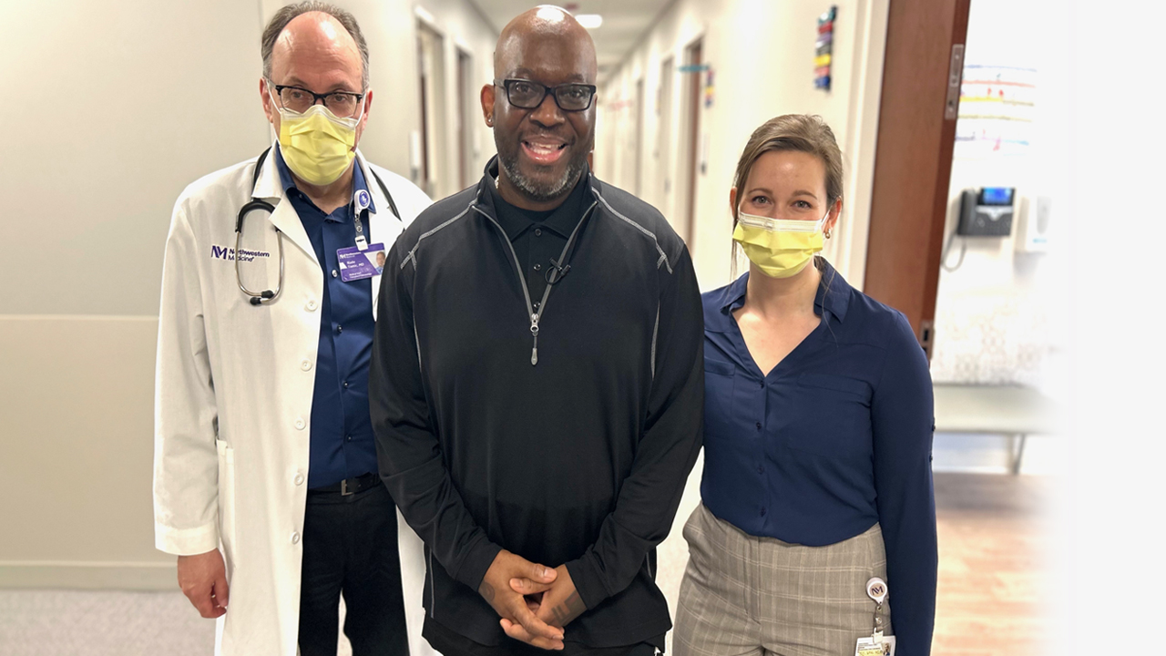 Art Gillespie in street clothes standing with his physician and nurse in a hospital corridor.