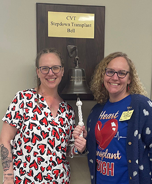 Meredith Everhart (left) and Abbey Cannon (right) stand in front of the transplant bell smiling. 