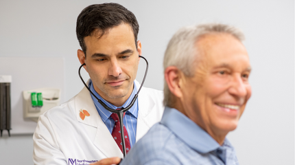 A Northwestern Medicine physician listening to the breathing of an elderly man who is smiling.