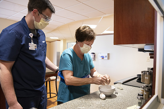 Patient is being assisted in cracking an egg into a bowl.