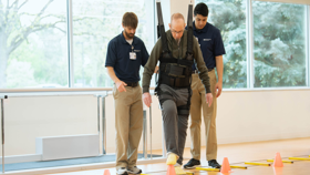 Two male clinicians helping a patient to walk using an assisted device.