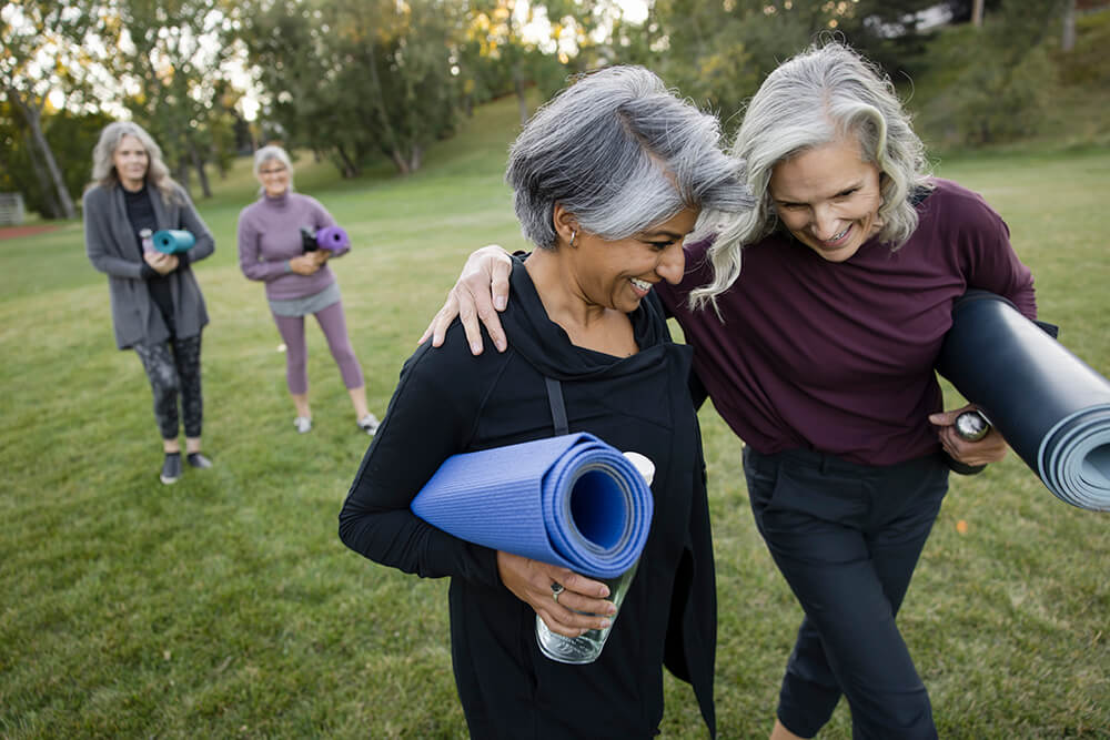Two women with grey hair holding yoga mats