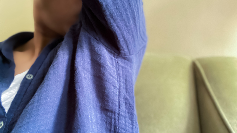 A person wearing a blue buttoned shirt smelling their armpit. 