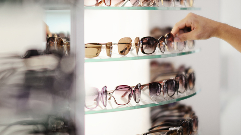 A person picking out sunglasses displayed on a store shelf. 