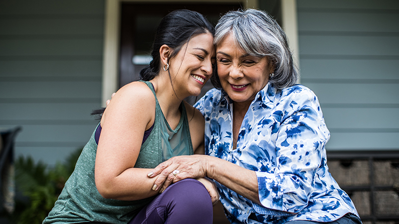 Two people embracing each other and smiling with a house in the background.