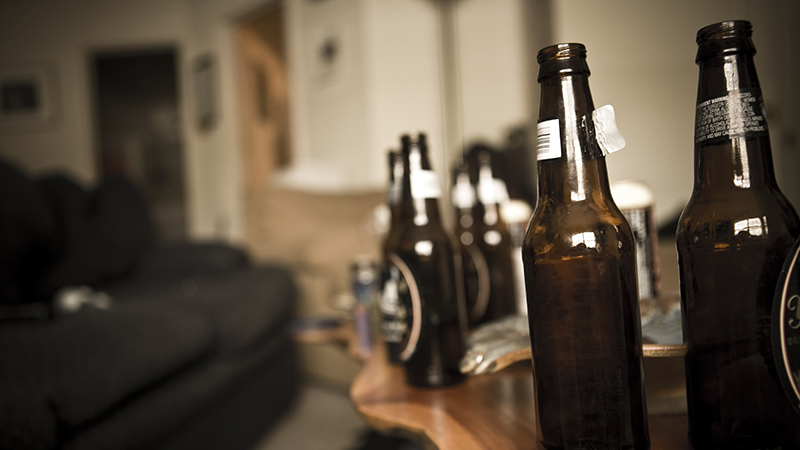 Bottles of open brown beer bottles on a wooden coffee table next to a brown sofa. 