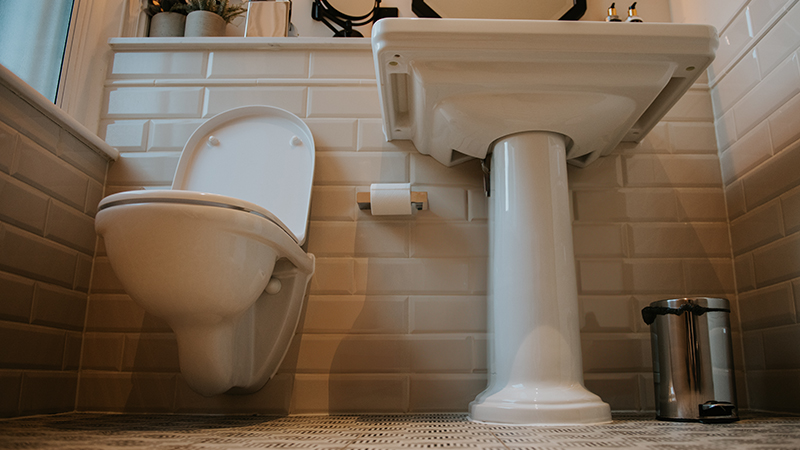 Picture taken at floor level of a sink and toilet in a white tiled bathroom. 