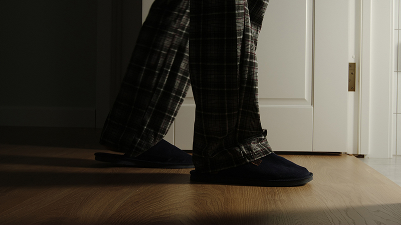 A person wearing pajamas and slippers, pictured from the shins down while they walk through a door at night. 