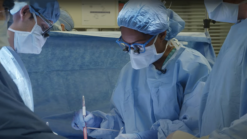 Surgeons wearing blue scrubs while performing a kidney transplant in an operating room.