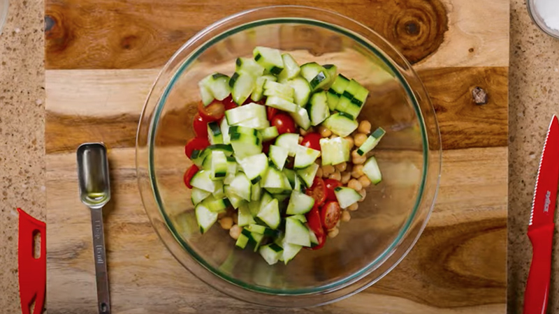 A cucumber tomato salad in a glass bowl, pictured from above. 
