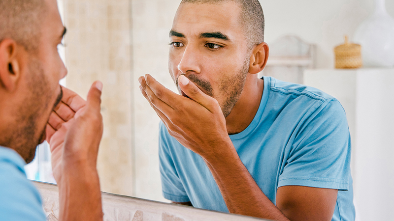 A person smelling their breath during morning grooming routine.