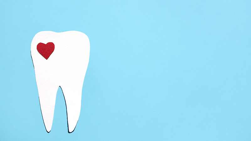 Cut paper illustration of a white tooth with a tiny red heart in the corner, on a blue background.