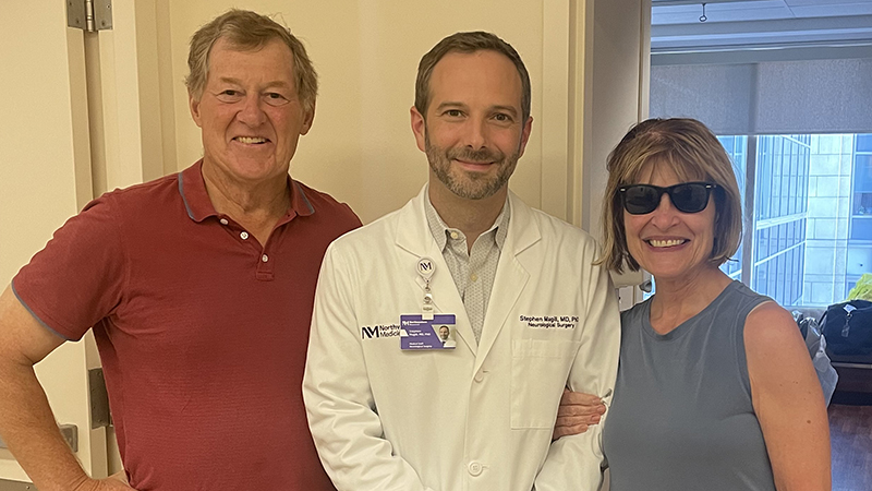 Mark Fenton, Steven T. Magill, MD, PhD, and patient Leslie Fenton stand together smiling at Northwestern Memorial Hospital. 