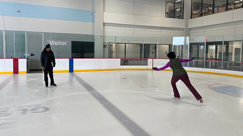 Two people ice-skate at an indoor rink.