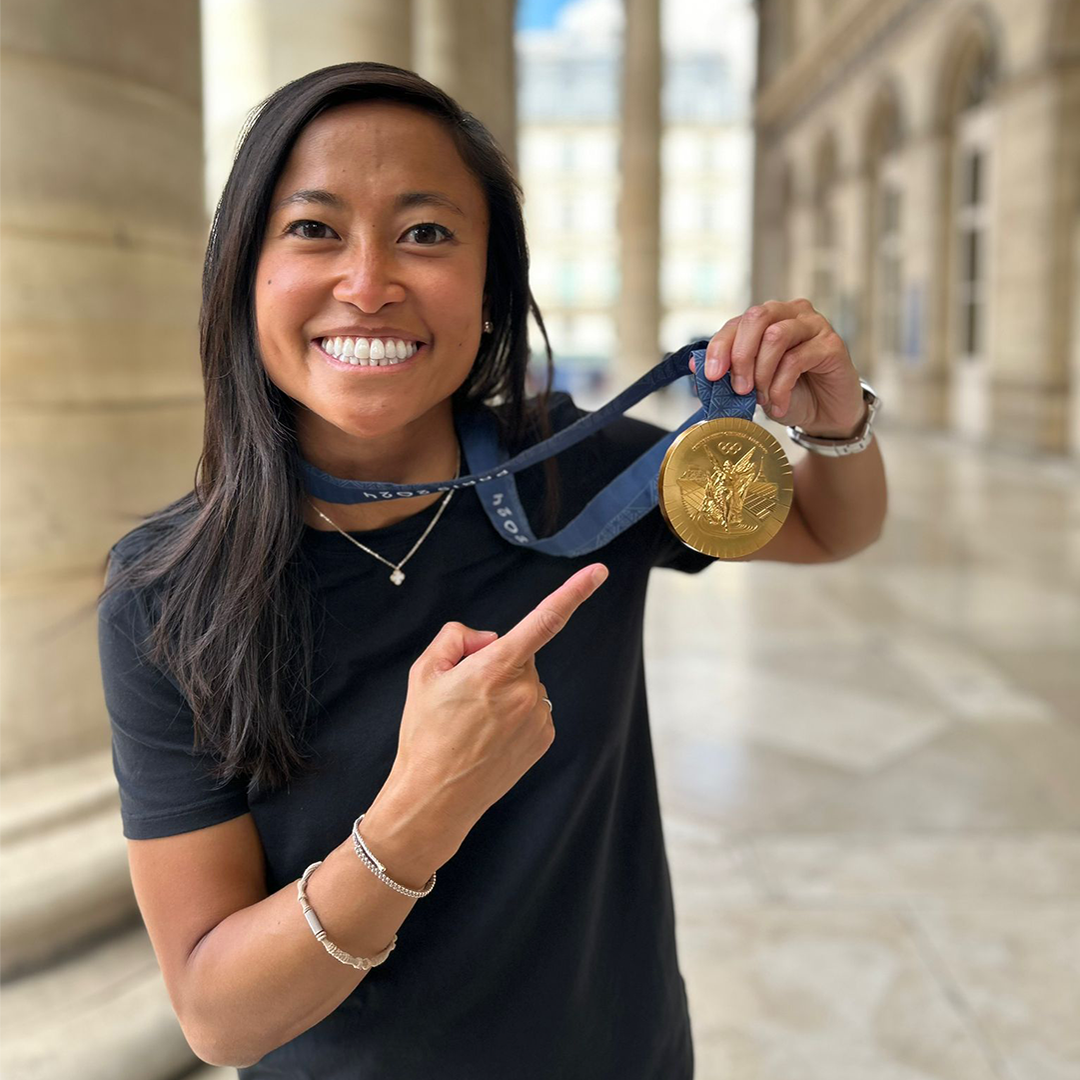 Physician pointing to her gold medal and smiling