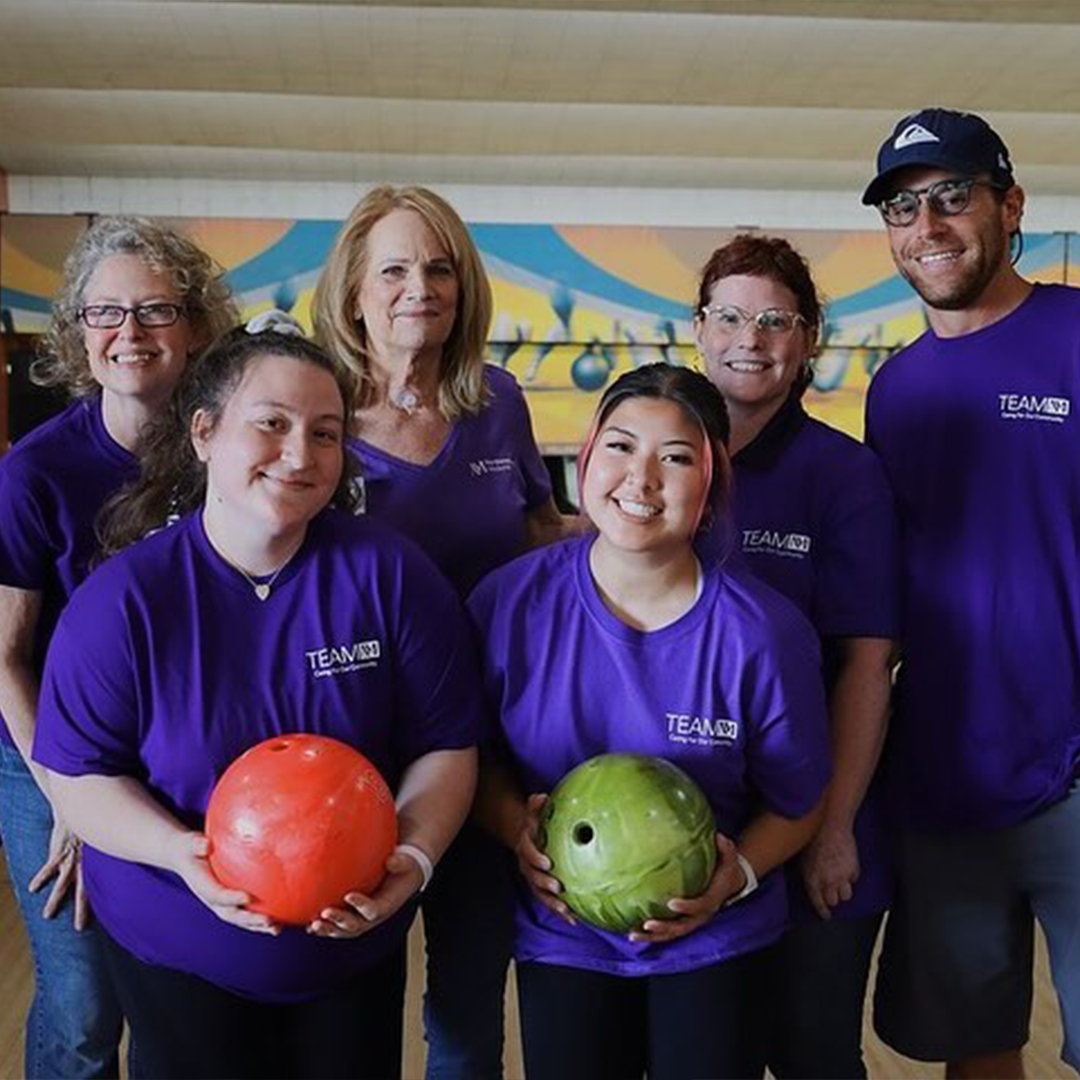 Team NM members posing with bowling balls in a bowling alley